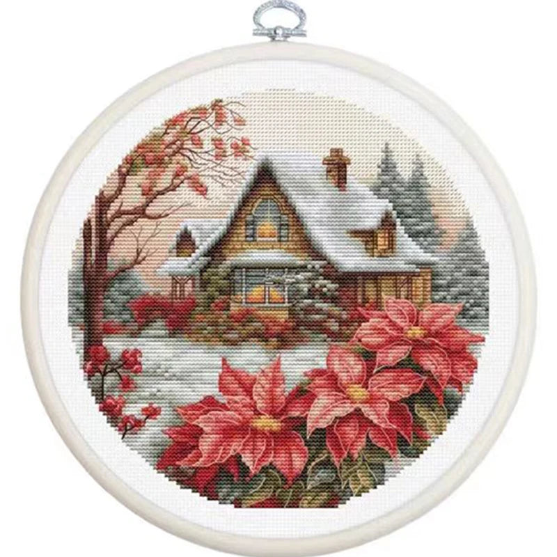 Cross-stitched scene of a snowy cabin with poinsettias in an embroidery hoop.