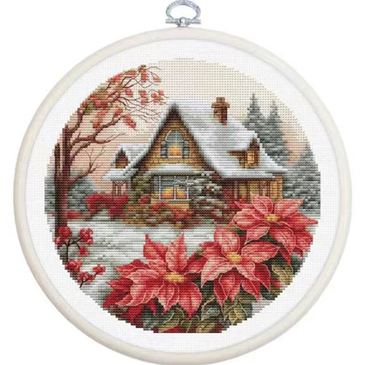 Cross-stitched scene of a snowy cabin with poinsettias in an embroidery hoop.