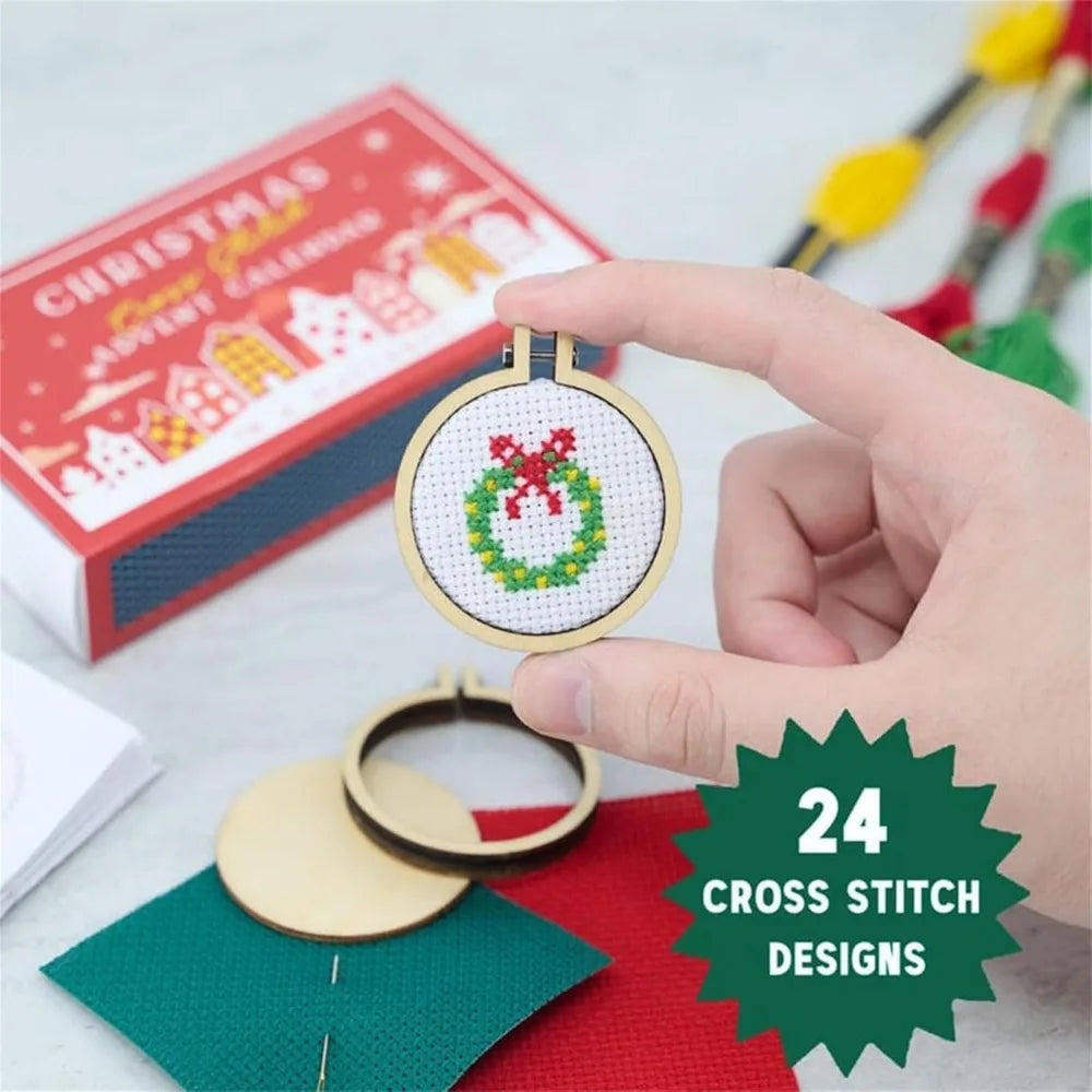 Hand holding a cross-stitched Christmas ornament with a box of craft materials in the background.