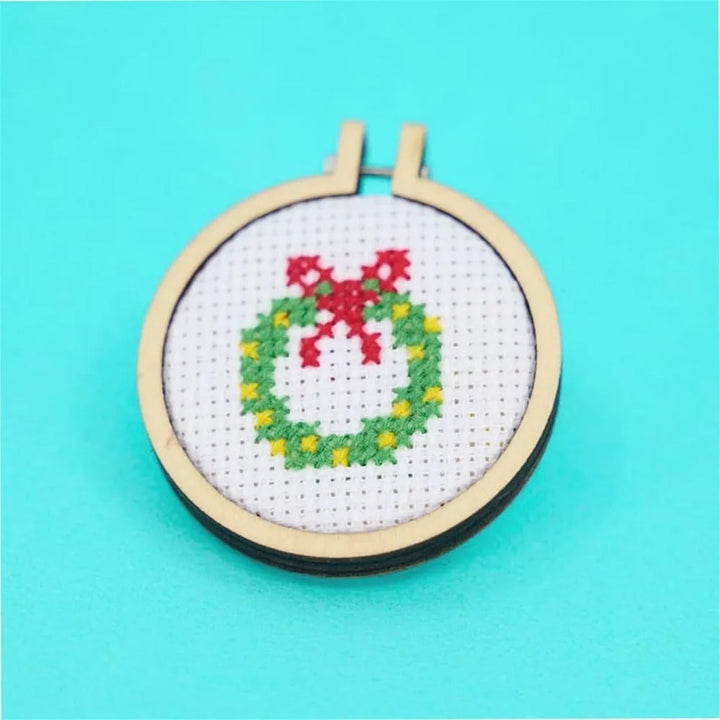 Cross-stitched wreath design in an embroidery hoop on a turquoise background