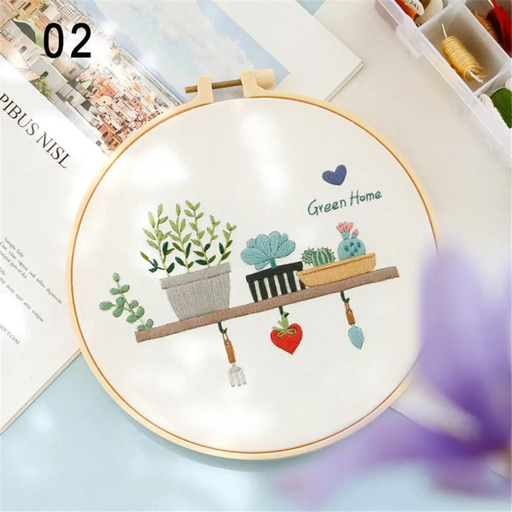 Embroidery hoop with a 'Green Home' design featuring plants and a chair on a table.