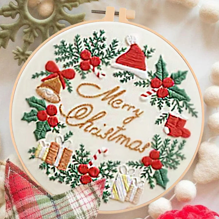 Embroidery hoop with Christmas-themed design featuring holly leaves, berries, and festive elements.