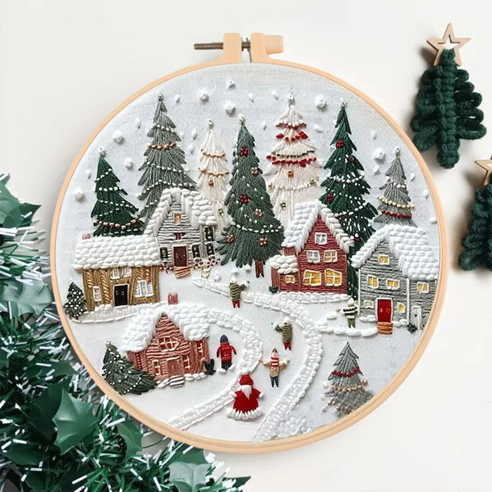 Embroidery hoop with a festive village scene surrounded by Christmas trees.
