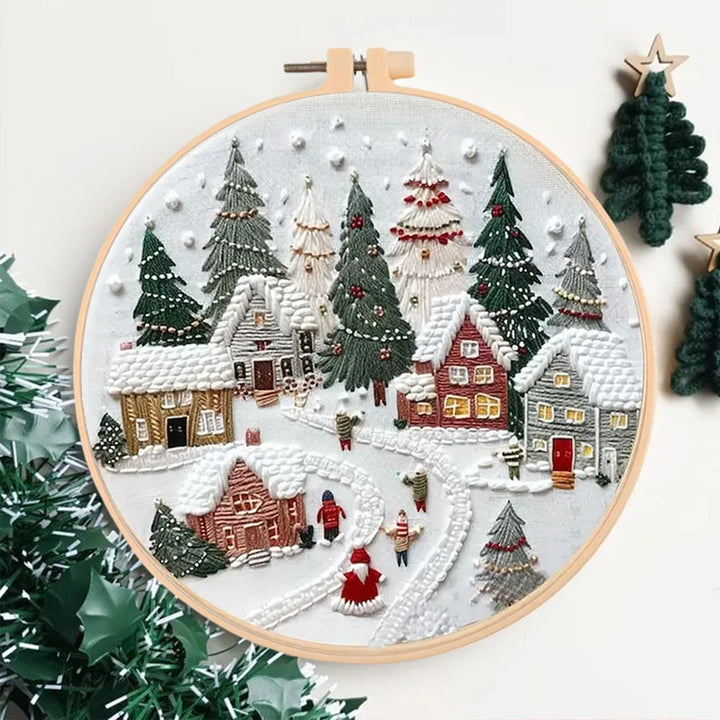 Embroidery hoop with a festive village scene surrounded by Christmas trees.