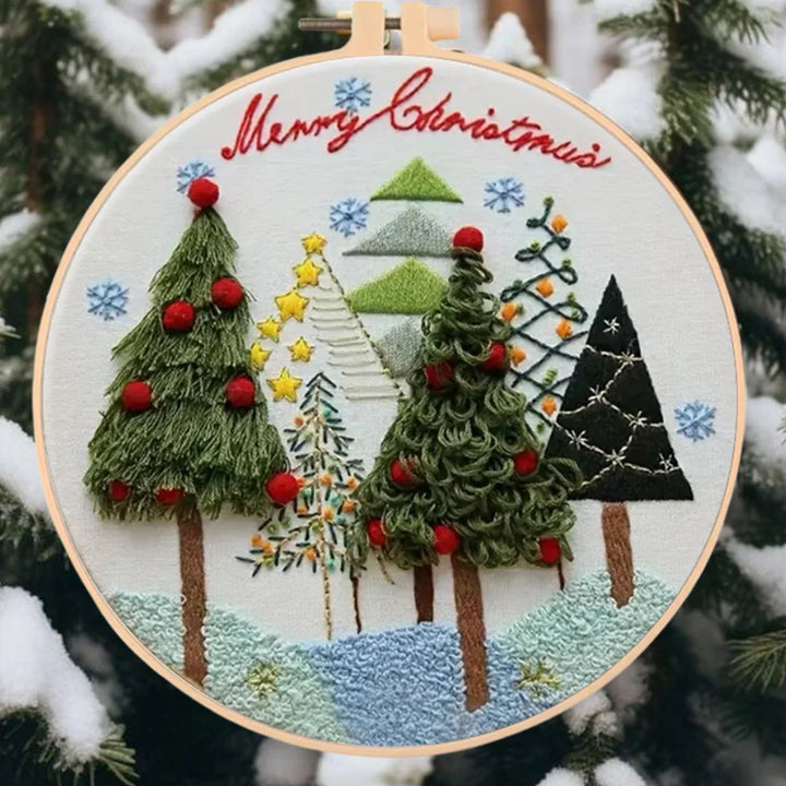 Embroidery hoop with Christmas-themed trees and 'Merry Christmas' text, against a snowy tree background.