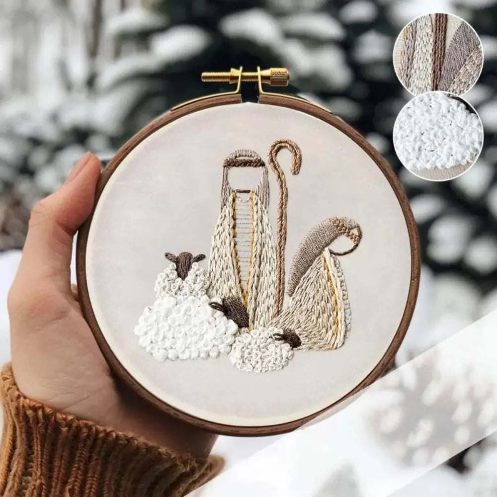 Embroidery hoop with winter-themed design of a sheep and shepherd's crook, held against a snowy background.
