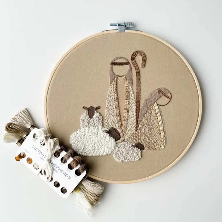 Embroidery hoop with embroidered design of a shepherd and sheep, accompanied by a small card labeled 'Native Shepherd's'.