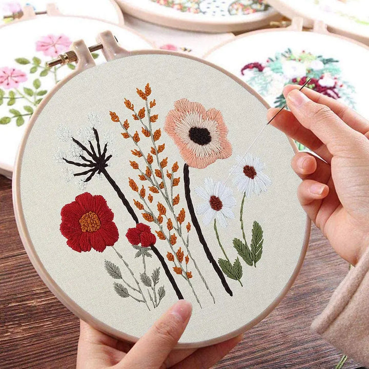 Embroidery hoop with floral design being worked on, held by a person.
