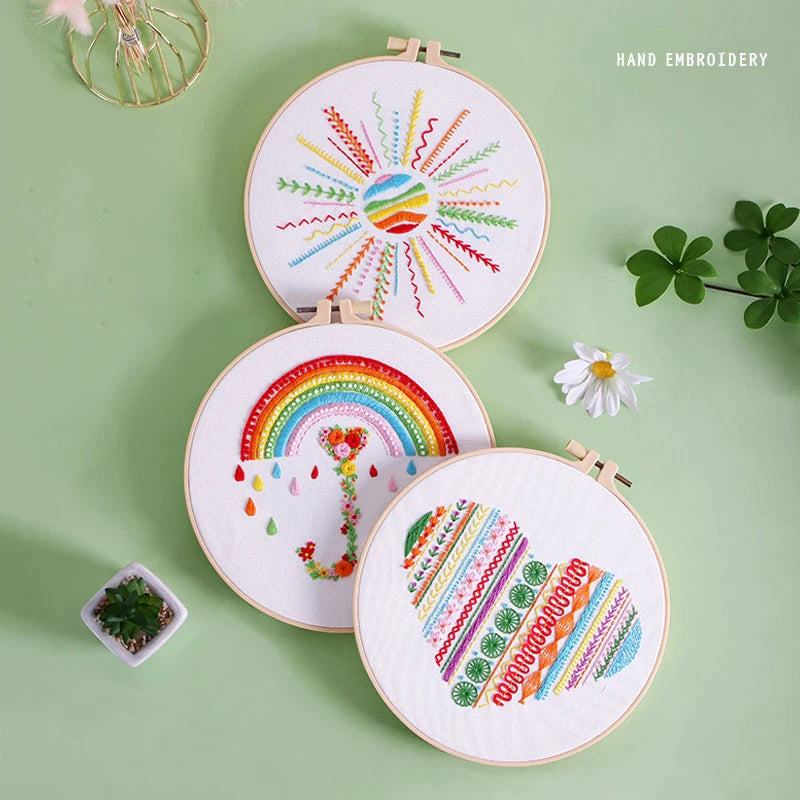 Three hand-embroidered hoops with colorful designs on a green background