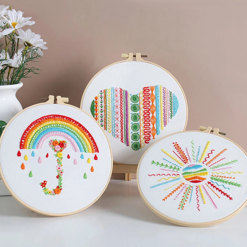 Three embroidery hoops with colorful patterns on a neutral background