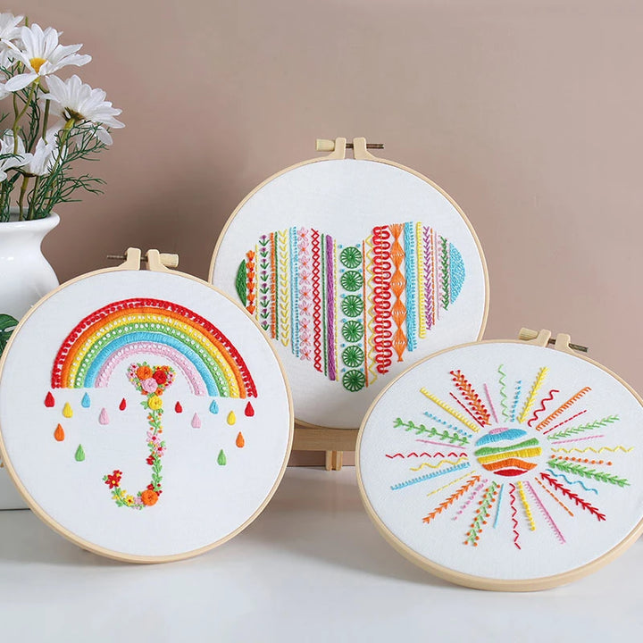 Three embroidery hoops with colorful patterns on a neutral background