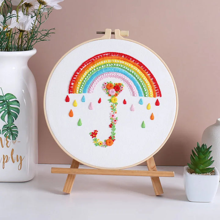 Embroidery hoop with a colorful rainbow and floral design on a stand against a beige wall.