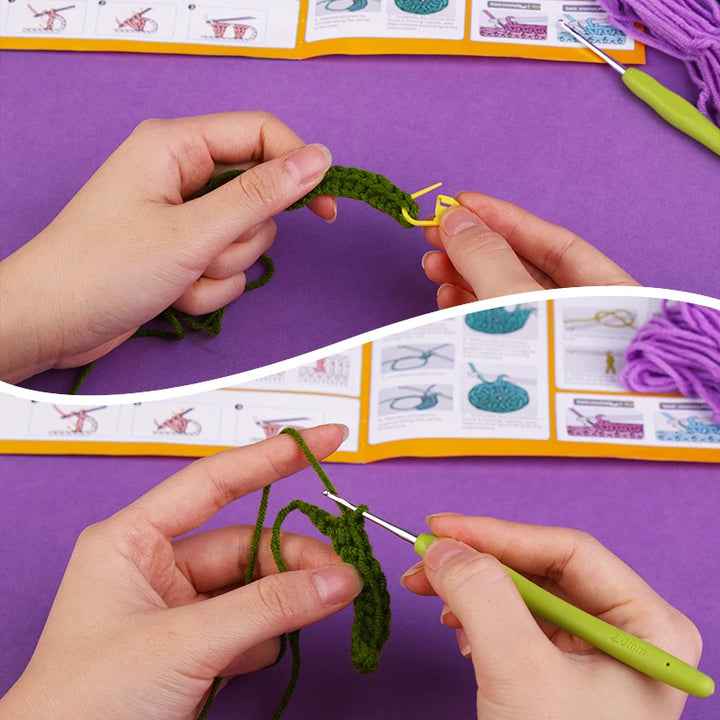 Hands crocheting with green yarn and a crochet hook on a purple surface with a patterned book in the background.