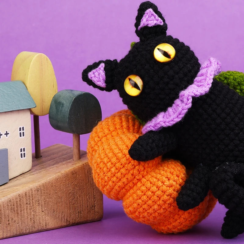 Crocheted black cat with yellow eyes holding an orange pumpkin against a purple background