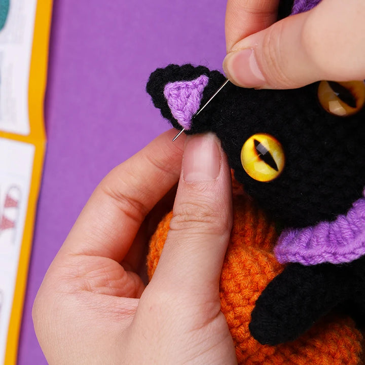 Handcrafting a black cat plush toy with purple accents on a purple background