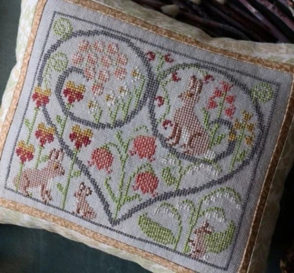 Decorative pillow with cross-stitched design of a fox and flowers on a textured surface.