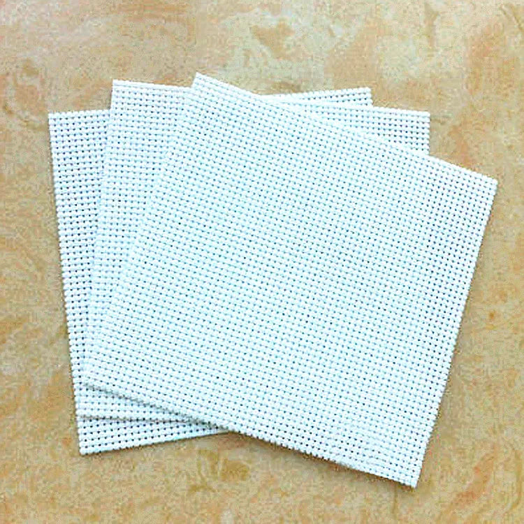Stack of white cross-stitching fabric sheets on a beige surface