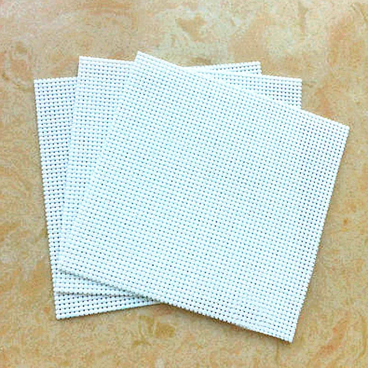 Stack of white cross-stitching fabric sheets on a beige surface