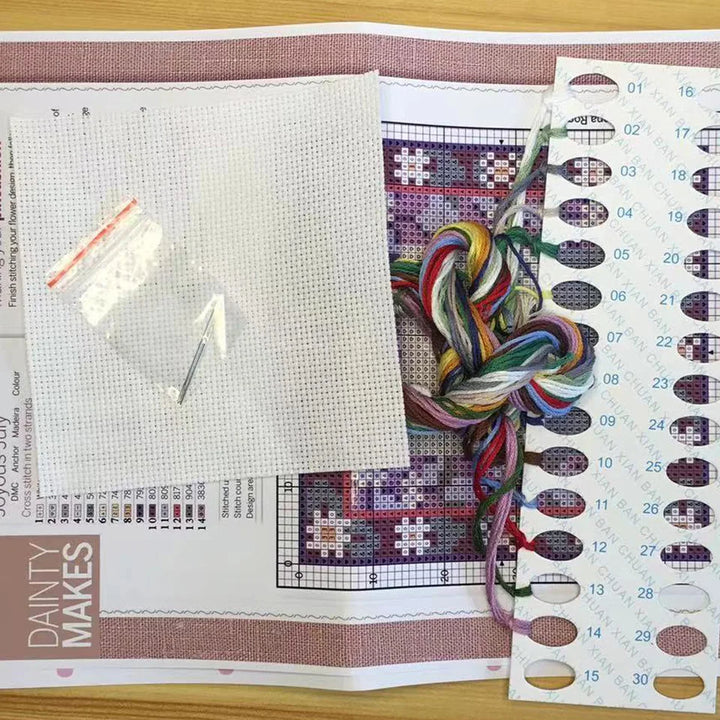 Cross-stitching kit with fabric, thread, needle, and pattern on a wooden surface