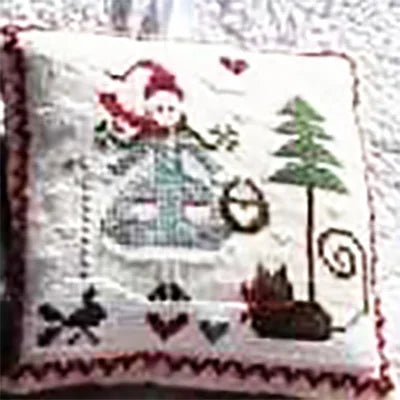 Decorative pillow with a cross-stitched design of a girl, tree, and cat on a white background.