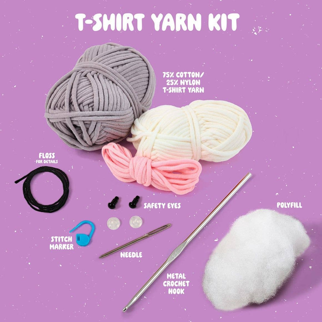 T-shirt yarn kit with yarn balls, safety eyes, needle, metal crochet hook, and other tools on a purple background.