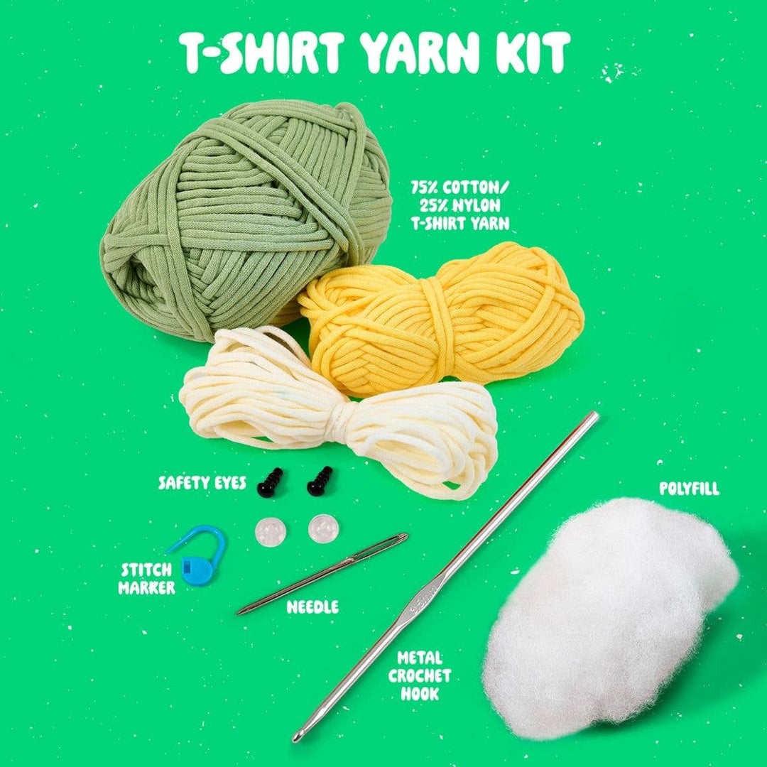 T-shirt yarn kit with yarn balls, safety eyes, needle, crochet hook, and polyfill on a green background.