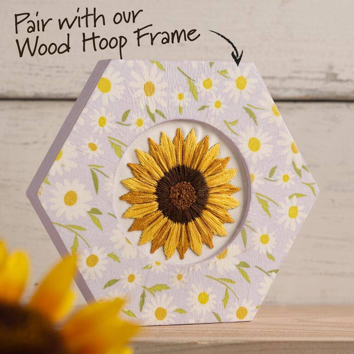 Hexagonal fabric piece with embroidered sunflower design on a wooden surface