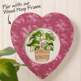 Heart-shaped frame with floral pattern containing an embroidered plant design, paired with a wood hoop frame.