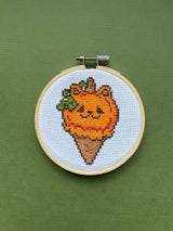 Cross-stitched design of a carrot with a face in an embroidery hoop on a green background