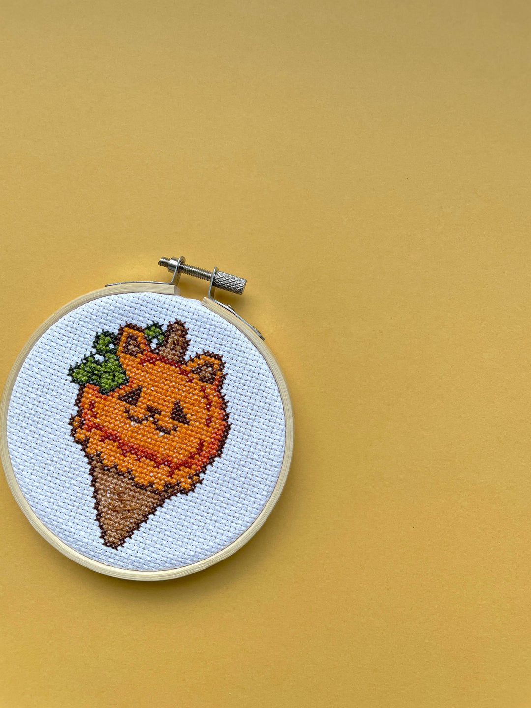 Embroidery hoop with a smiling carrot design on a mustard yellow background