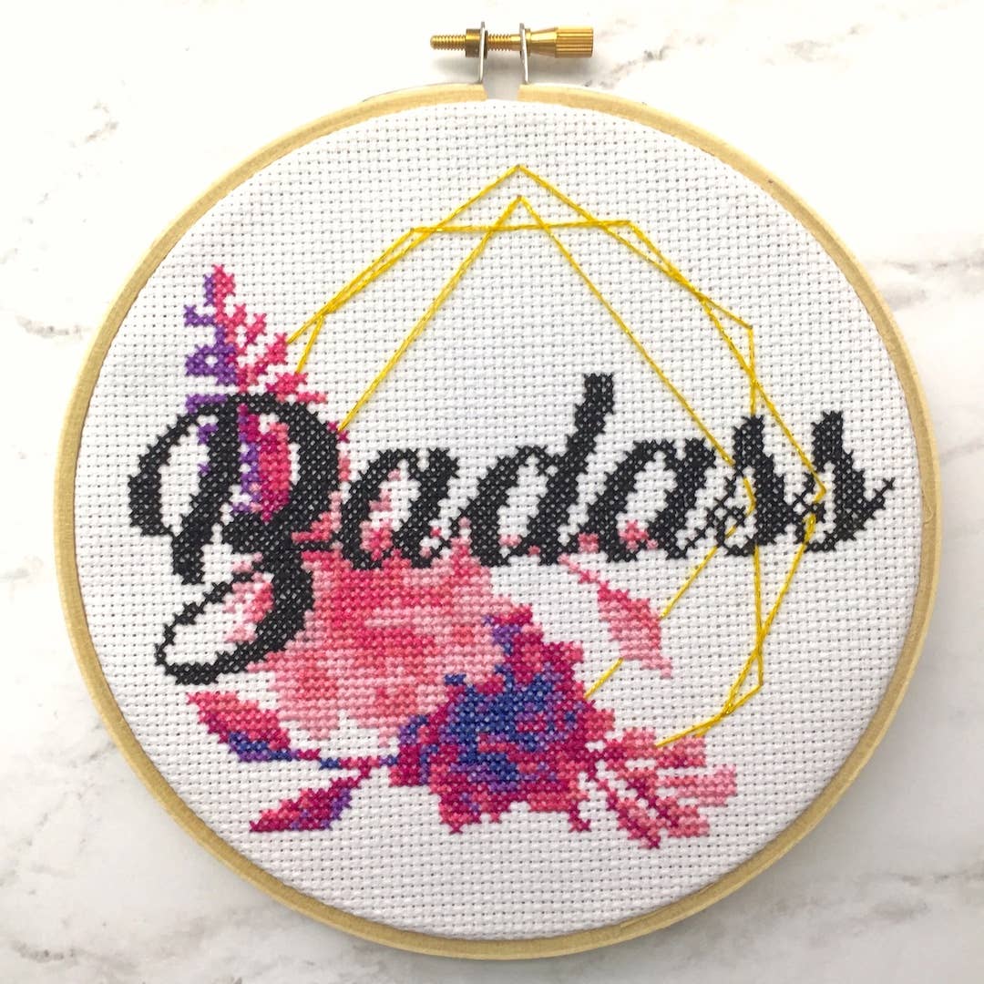 Cross-stitched hoop with 'Badass' and floral design on a white background