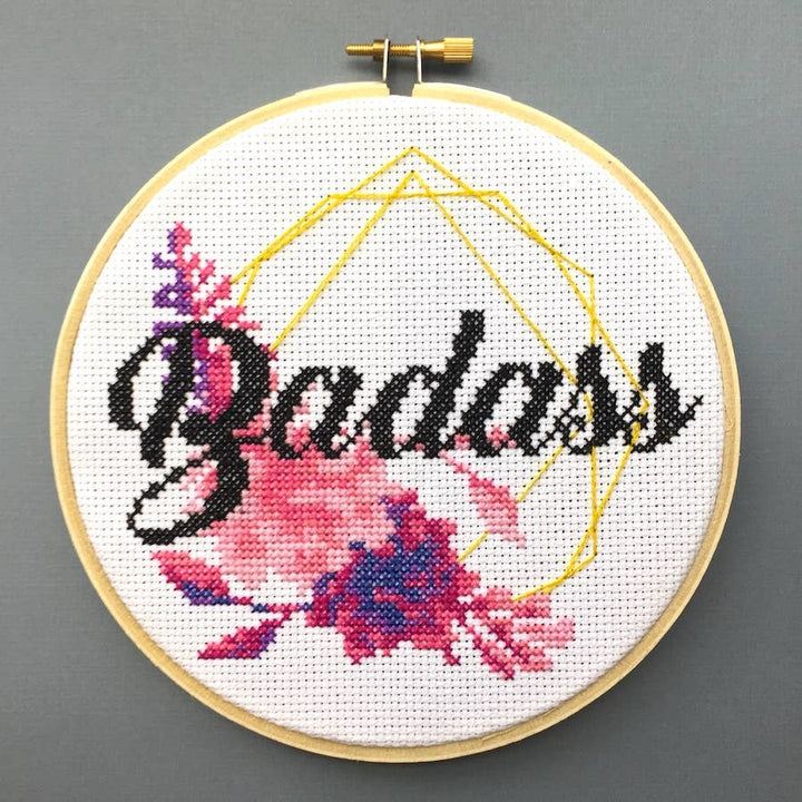 Cross-stitched hoop with 'Badass' and floral design on a gray background