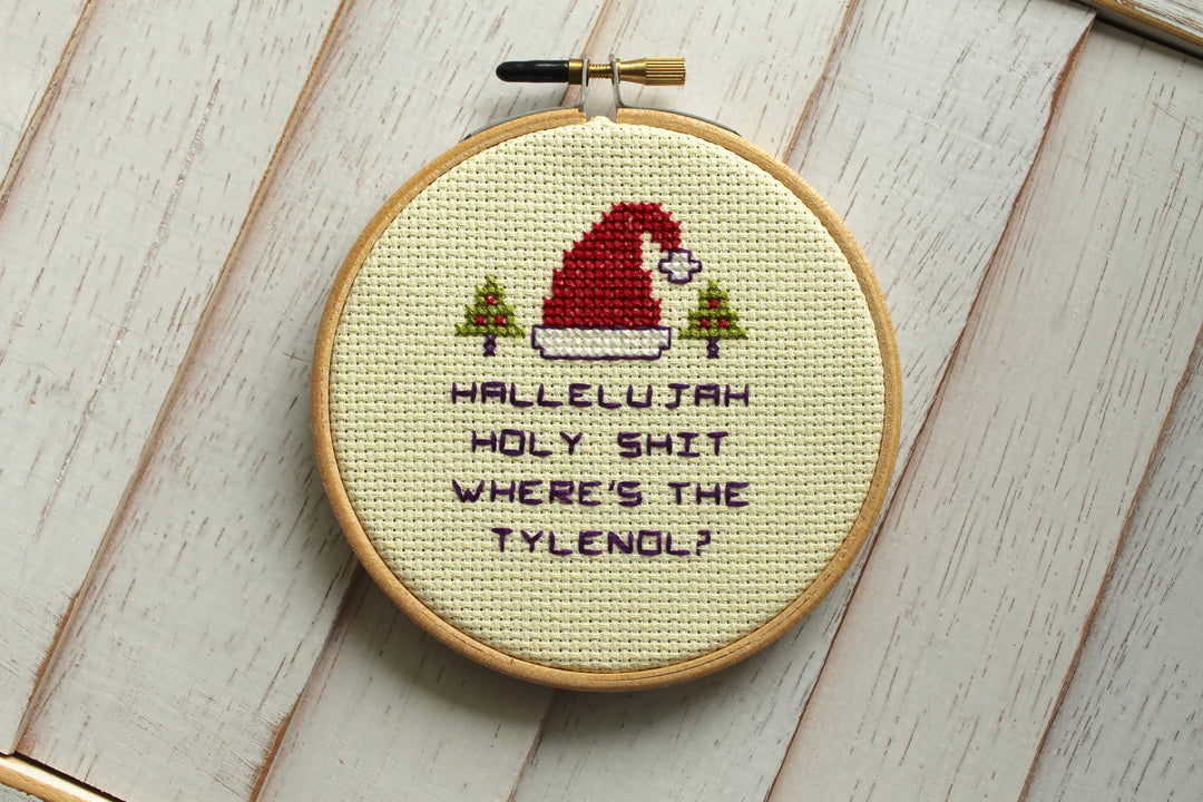Cross-stitched hoop with humorous text and Santa Claus design on a wooden surface