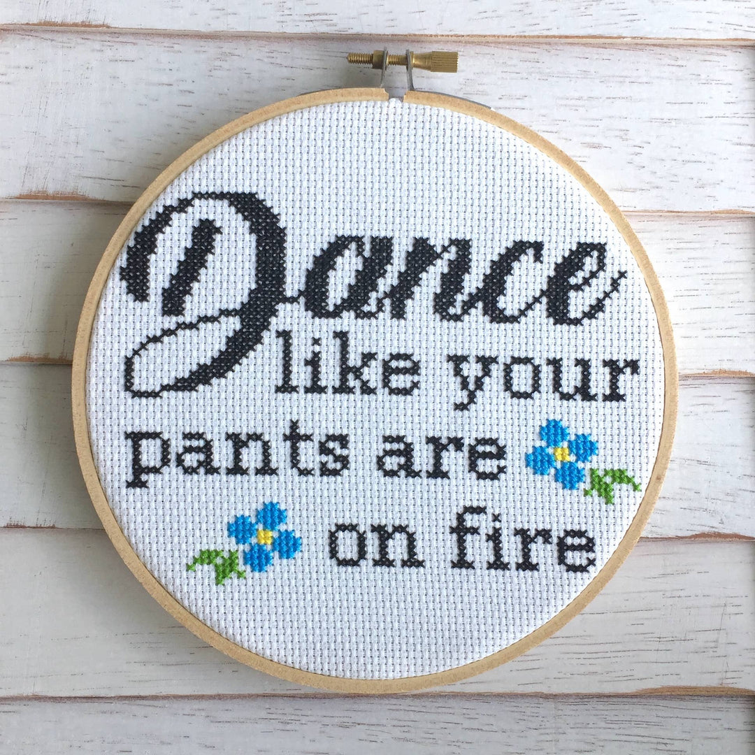 Cross-stitched hoop with 'Dance like your pants are on fire' text and flowers on a wooden background