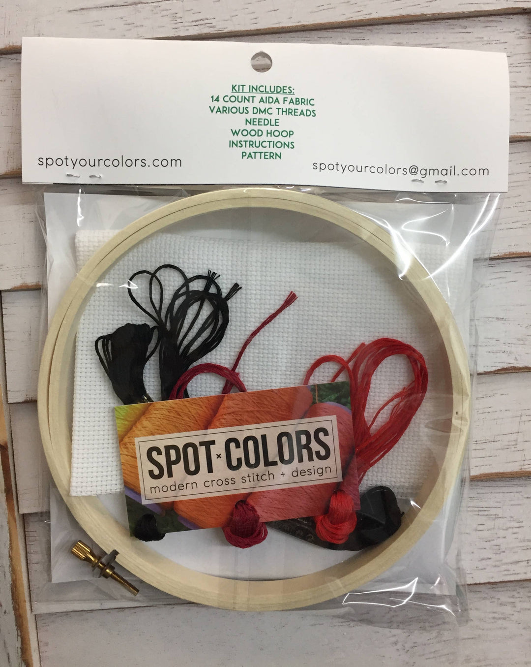 Embroidery hoop with cross-stitch kit including fabric, threads, and hoop on a wooden surface.