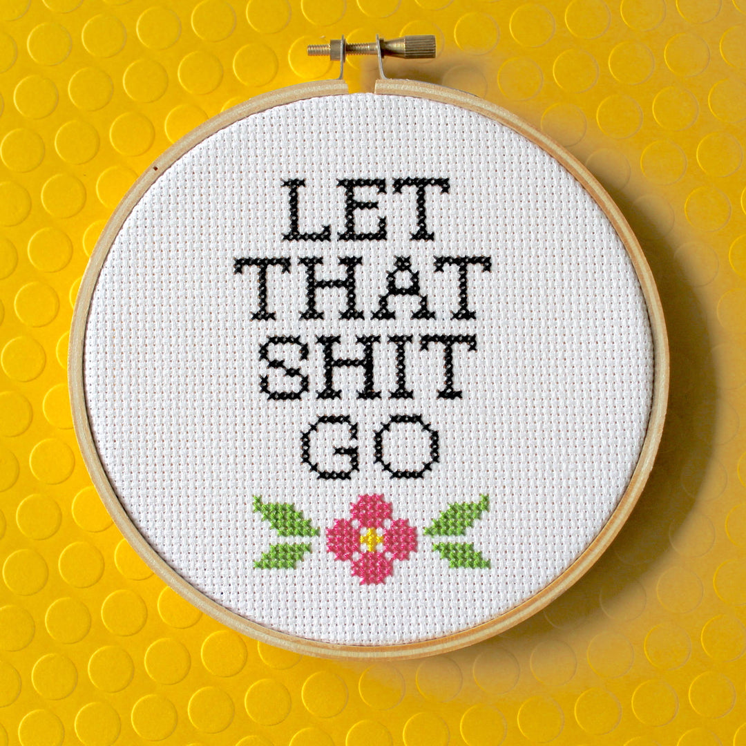 Cross-stitched hoop with text 'LET THAT SHIT GO' on a yellow background