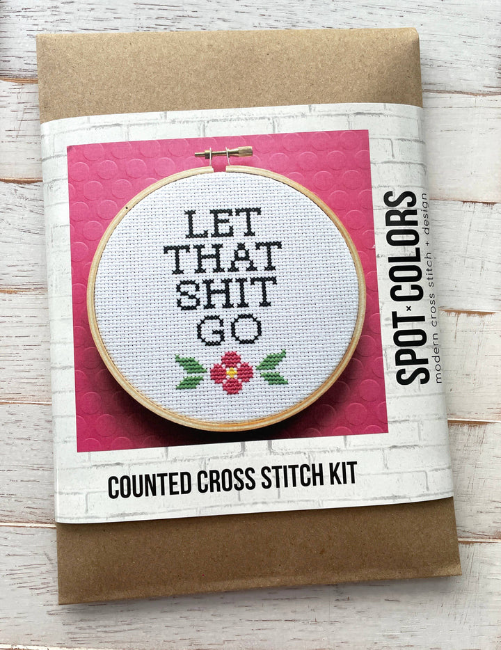 Cross stitch kit with text 'LET THAT SHIT GO' on a pink background, featuring Spot Colors branding.