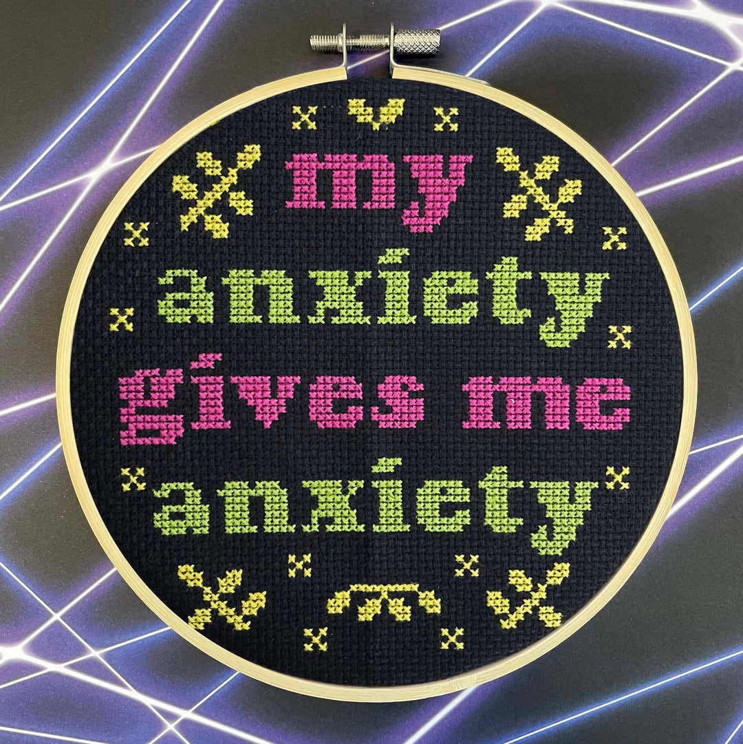 Cross-stitched hoop with colorful text on a dark background