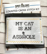 Cross stitch kit with 'My cat is an ass' text on a wooden surface