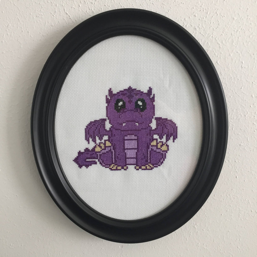Framed cross-stitched purple dragon on a white background