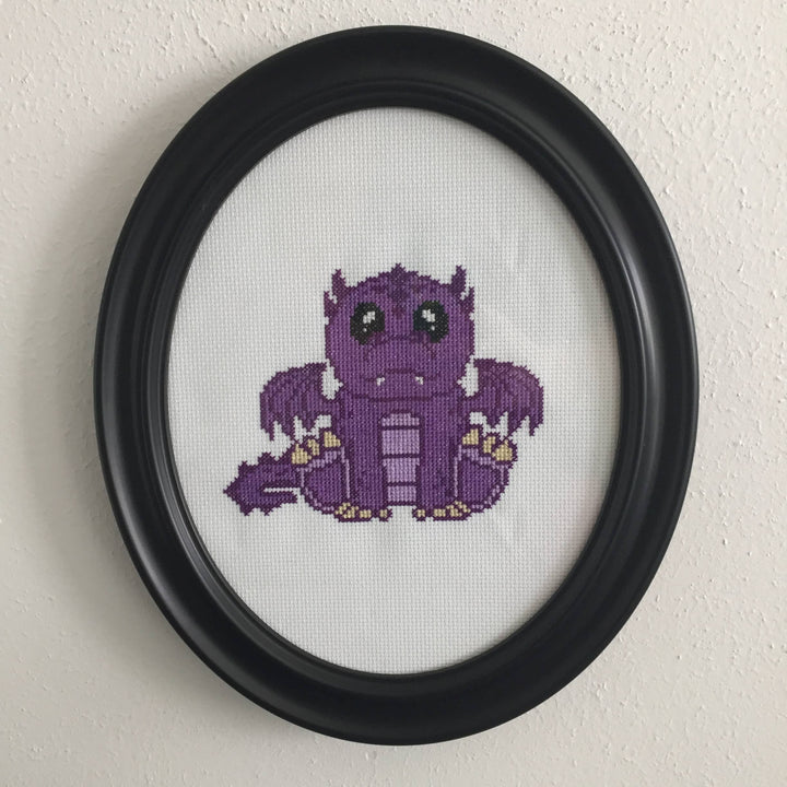 Framed cross-stitched purple dragon on a white background