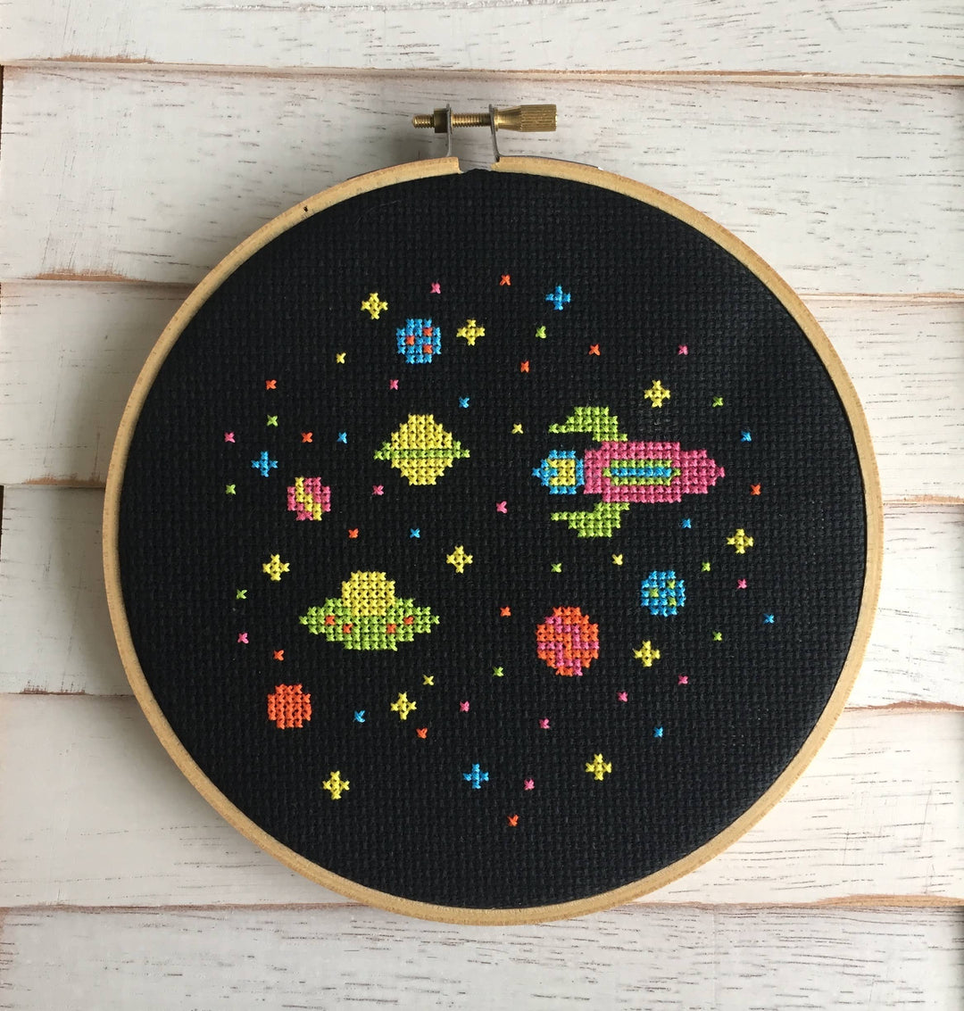 Embroidery hoop with colorful space-themed cross stitch on a wooden surface