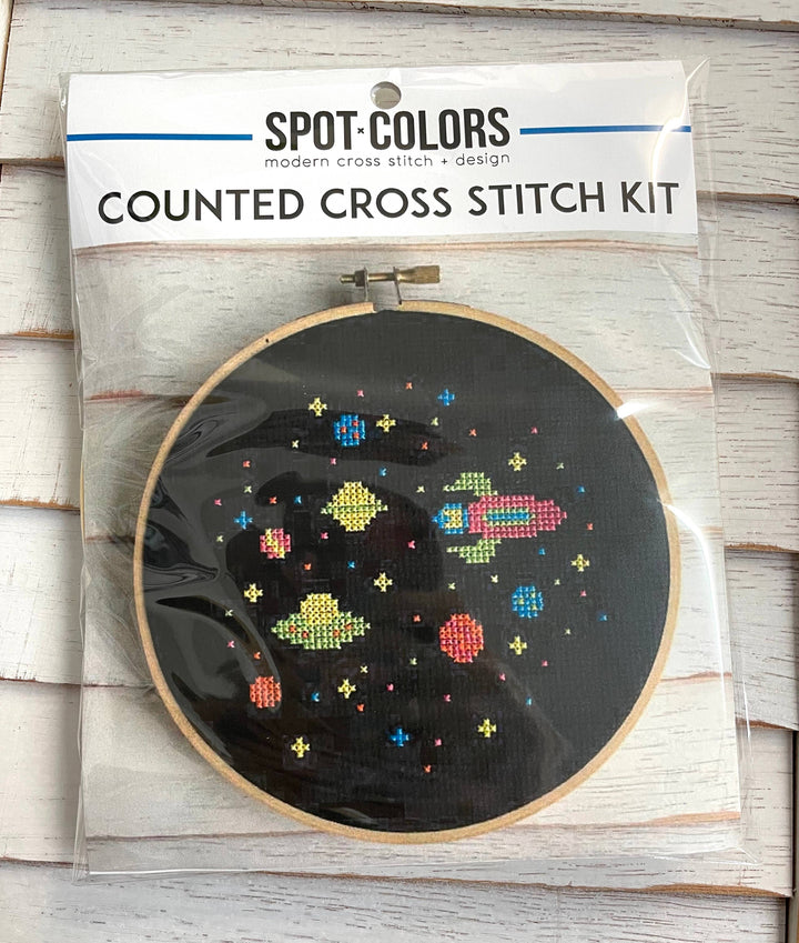 Counted cross stitch kit with space-themed design on a wooden surface
