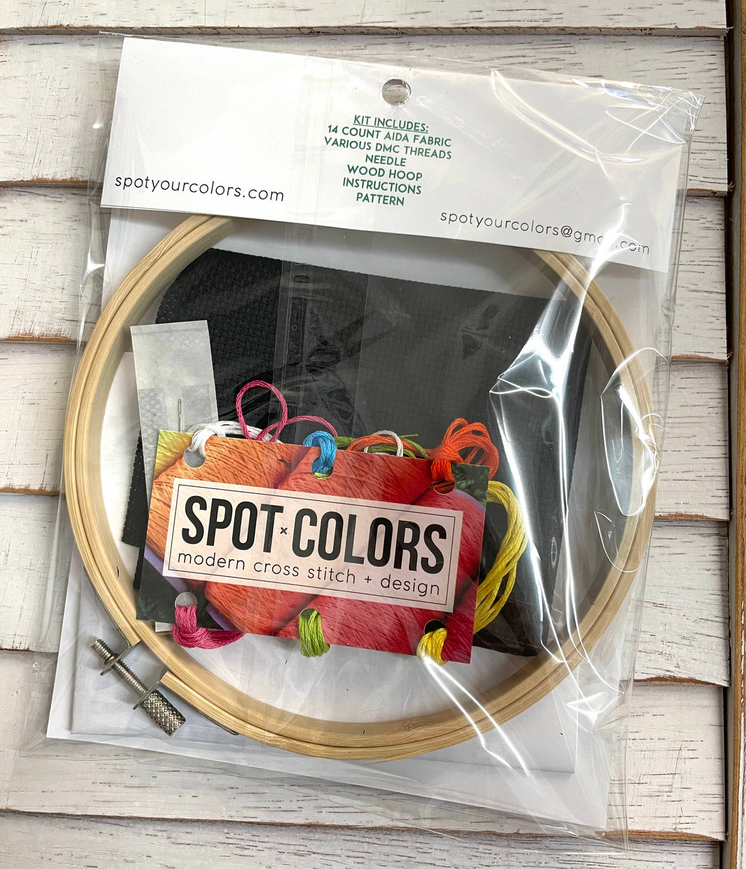Embroidery hoop with cross-stitch design kit and 'Spot Colors' branding on a wooden surface.