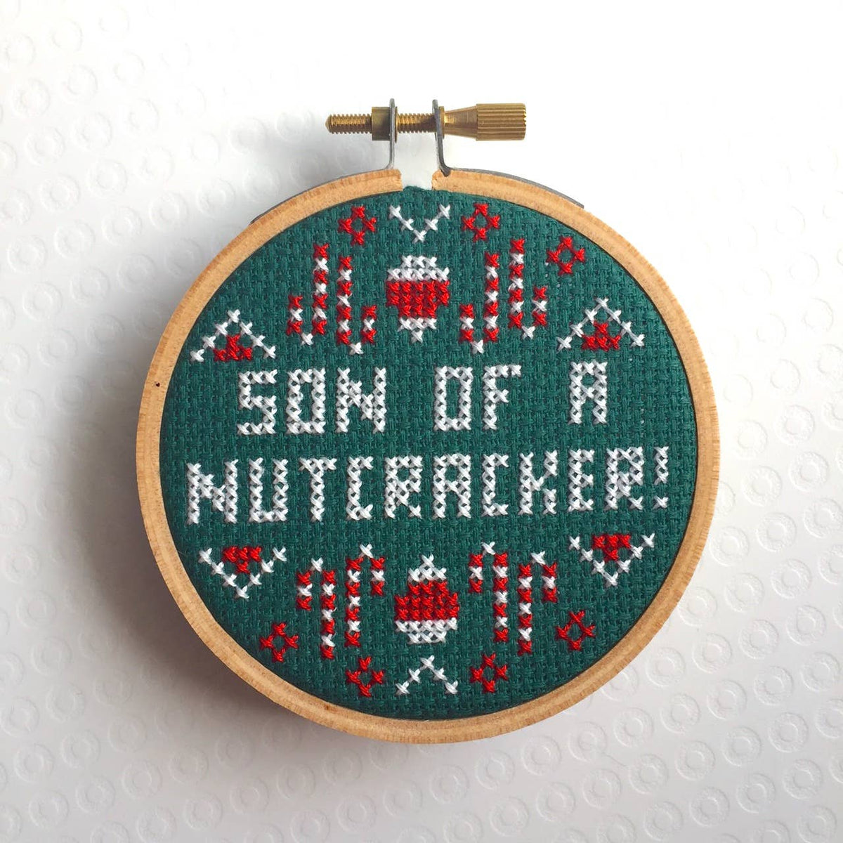 Embroidery hoop with cross-stitched design reading 'Son of Nutcracker!' on a white background