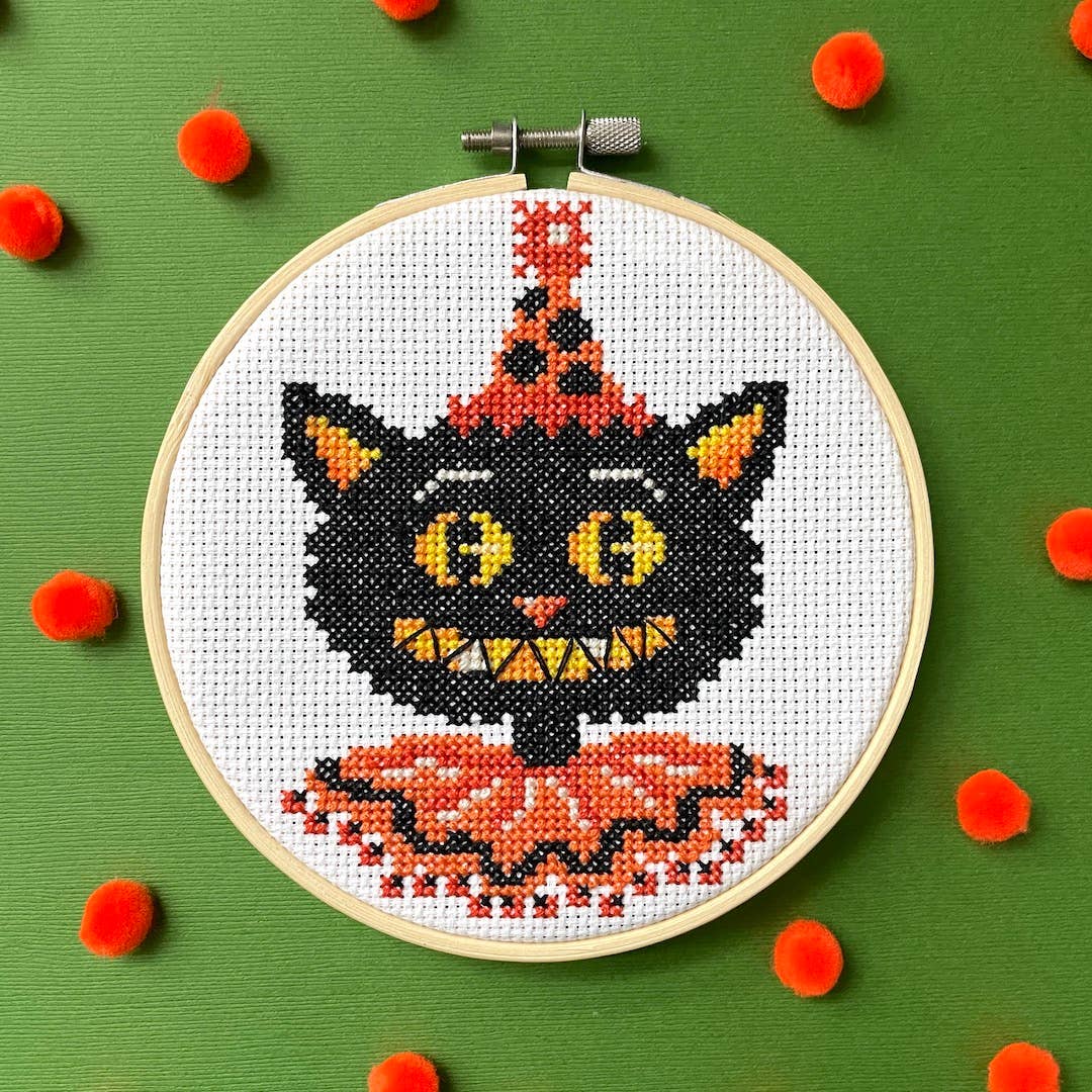 Embroidery hoop with a black cat design on a green background with red pom-poms.