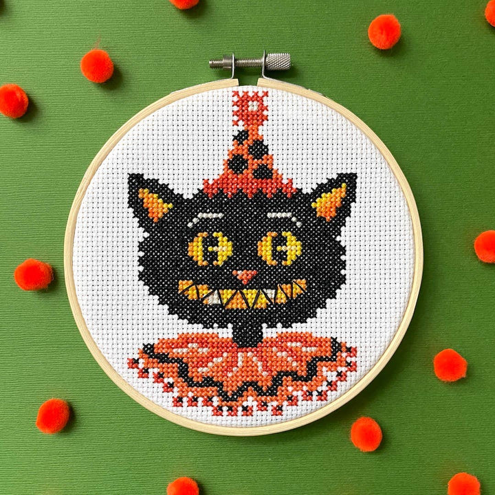 Embroidery hoop with a black cat design on a green background with red pom-poms.