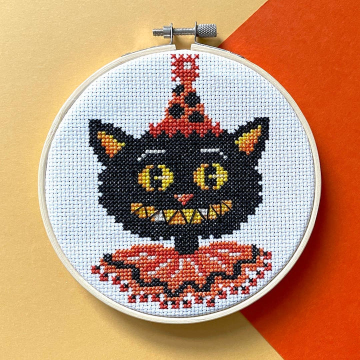 Cross-stitched black cat with a party hat on a white background