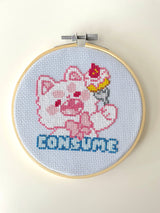 Cross-stitched design of a cartoon character with a cake on its head in an embroidery hoop.