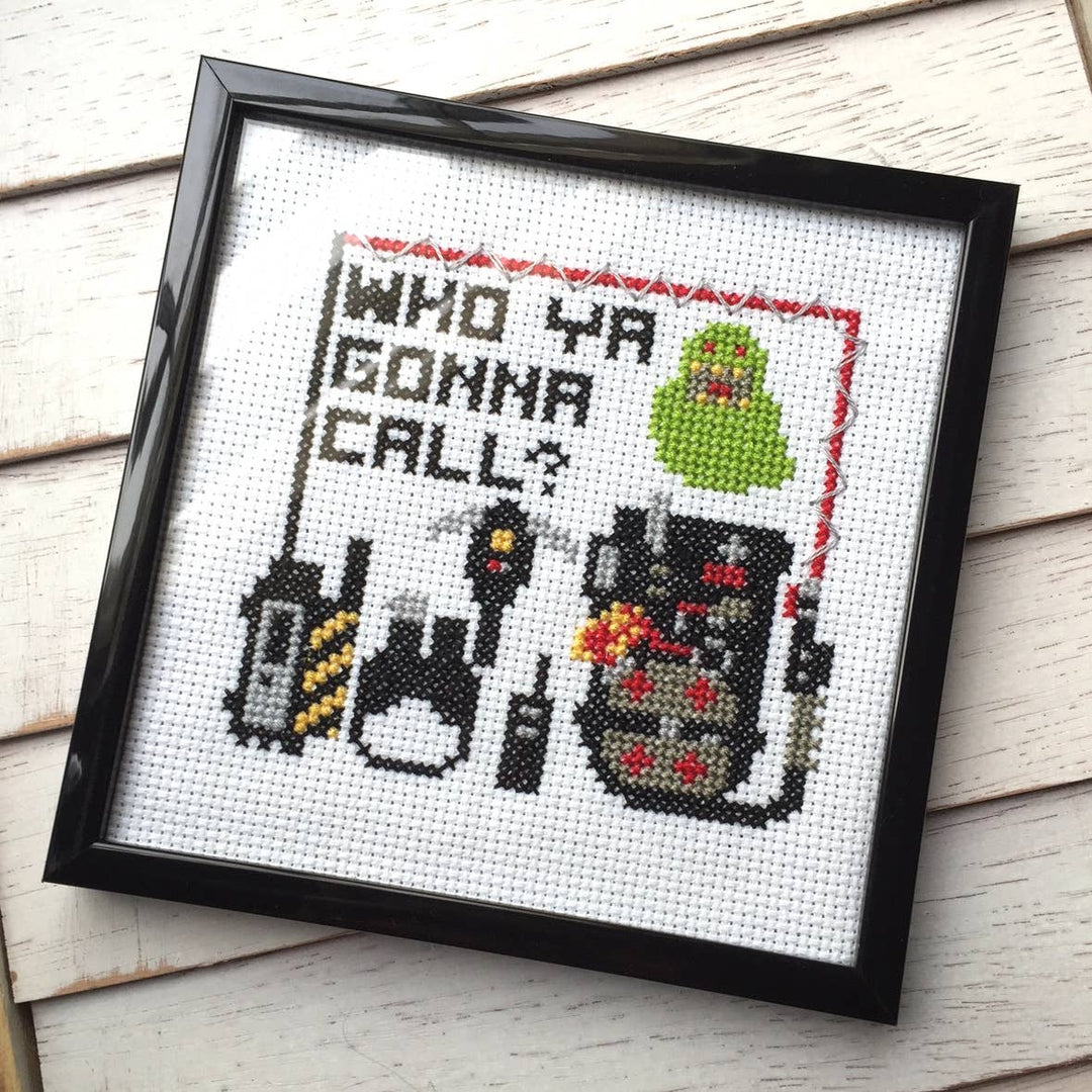 Framed cross-stitched artwork with text and character designs on a wooden surface